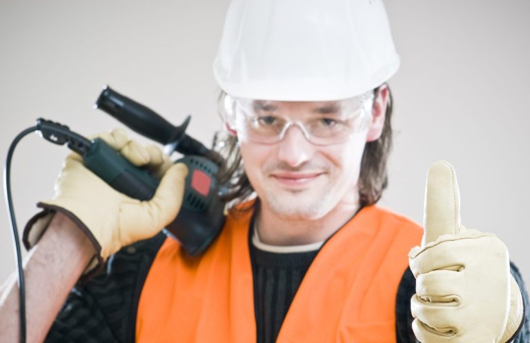 Mann in Sicherheitskleidung mit Schutzbrille, hält ein Werkzeug und zeigt Daumen hoch.